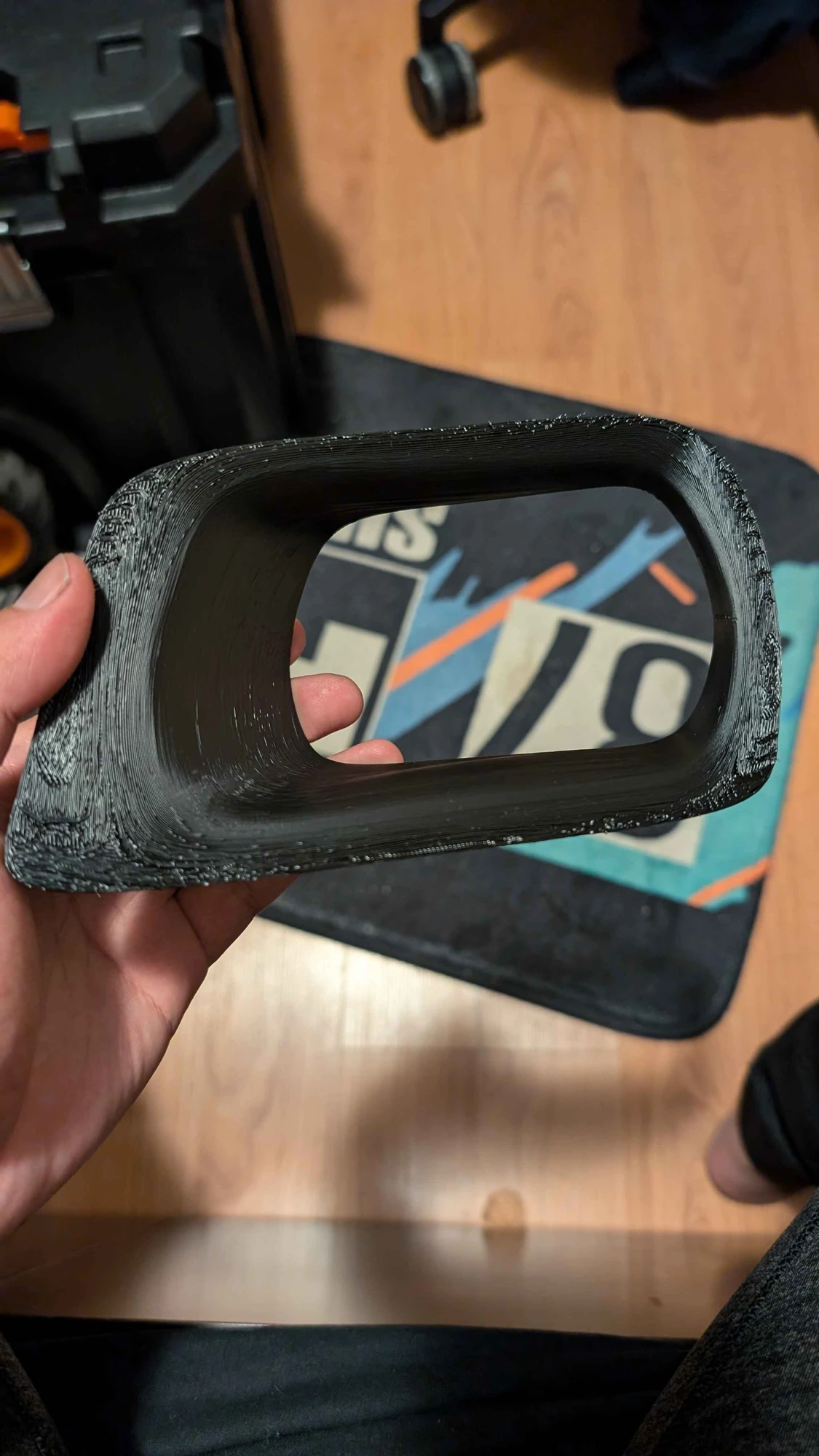 The printed black R34 headlight duct held in a hand, showing its rectangular opening and mounting perimeter.